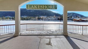 Eine überdachte Aussichtsplattform mit einem Schild, das 'LAKESHORE' zeigt, einem Holzdeck und Blick auf eine verschneite Landschaft mit Gebäuden und Bergen.