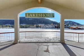 Eine überdachte Aussichtsplattform mit einem Schild, das 'LAKESHORE' zeigt, einem Holzdeck und Blick auf eine verschneite Landschaft mit Gebäuden und Bergen.