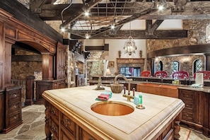Eine Küche mit einer großen Kochinsel, Steinwänden, Holzschränken und einem Chandelier.