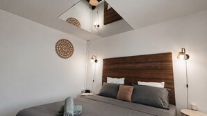 A modern bedroom with a wooden headboard, a large bed, two bedside lamps, and a circular wall decoration.