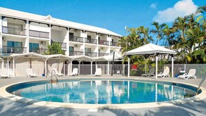 A hotel with a swimming pool, lounge chairs, and a covered seating area.