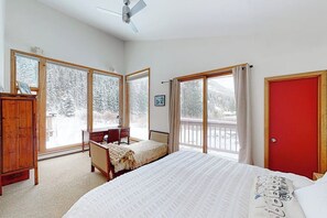 Ein Schlafzimmer mit Bett, Schreibtisch, Stuhl, Kleiderschrank und großen Fenstern mit Blick auf verschneite Bäume.