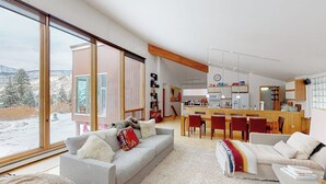 Uma sala de estar moderna com sofá, mesa de centro e vista para uma paisagem nevada através de grandes janelas.