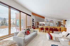 Ein modernes Wohnzimmer mit einer Couch, einem Couchtisch und Blick auf eine verschneite Landschaft durch große Fenster.