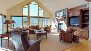 Un salon spacieux avec un haut plafond, de grandes fenêtres, une cheminée en pierre et des meubles en bois.