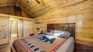 Une pièce de style cabane en bois, comprenant un lit, une table de chevet et une porte donnant sur une autre pièce.