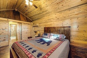 Ein Holzhütten-Zimmer mit einem Bett, einem Nachttisch und einer Tür zu einem weiteren Raum.