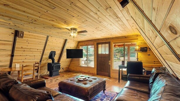 Un intérieur de chalet chaleureux avec un plafond en bois, une cheminée, un téléviseur, des canapés en cuir et un coin repas.