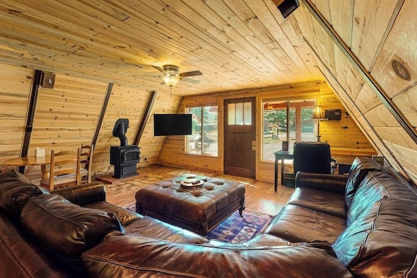 Ein gemütliches Blockhausschlafzimmer mit Holzbalkendecke, Kamin, Fernseher, Ledersofas und einem Essbereich.