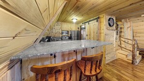 L’intérieur d’un chalet en bois comprend une cuisine, un coin bar et une horloge murale.