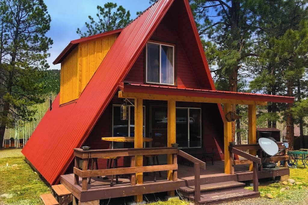 Une cabane rouge et jaune avec un porche, une antenne parabolique et une terrasse en bois.