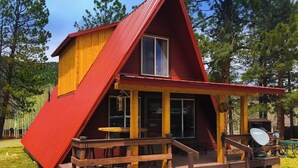 Une cabane rouge et jaune avec un porche, une antenne parabolique et une terrasse en bois.