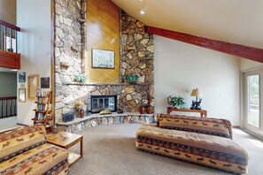 A living room with a stone fireplace, a bookshelf, and patterned sofas. - Charming Mountain View Condo with WiFi, Fireplace (Silverthorne)