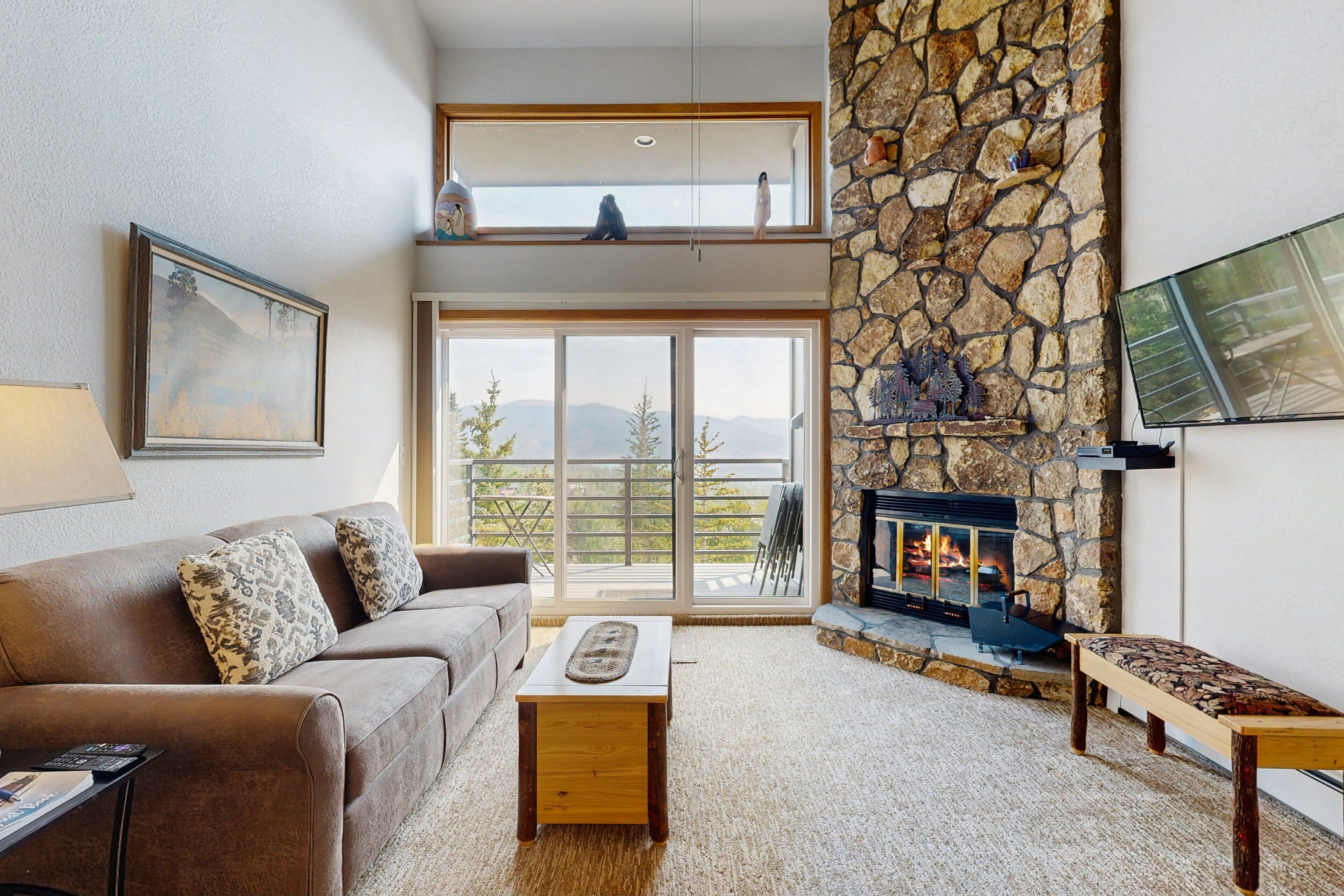 A living room with a stone fireplace, a sofa, a coffee table, and a TV mounted on the wall.