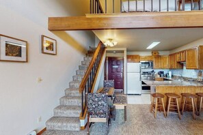 A staircase leading to a second floor, a kitchen with wooden cabinets, a dining area with a table and chairs, and a bar area with stools. - Charming Mountain View Condo with WiFi, Fireplace (Silverthorne)
