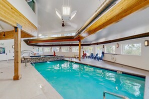 An indoor swimming pool with clear blue water, wooden beams, and a ceiling fan. - Charming Mountain View Condo with WiFi, Fireplace (Silverthorne)