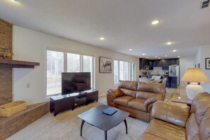 A living room with a fireplace, a television, leather sofas, and a kitchen in the background. - Modern Mountain View Hideaway w/ Spacious Deck & Free WiFi - Close to Skiing (Silverthorne)