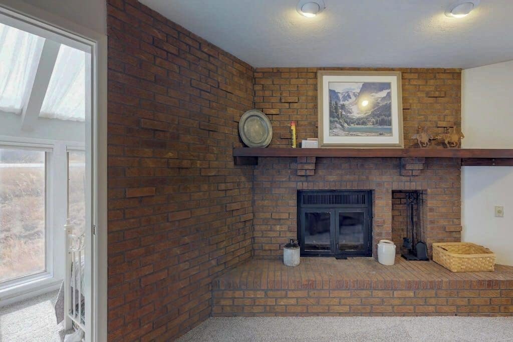 A corner room with a brick fireplace, a framed picture above it, and a shelf with decorative items.