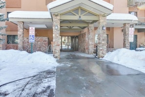 A hotel entrance with stone pillars, a covered walkway, and snow on the ground. - Ski-in/Ski-Out, Outdoor Pool, Hot Tub, Tennis, Sauna, & Gym (Steamboat Springs)