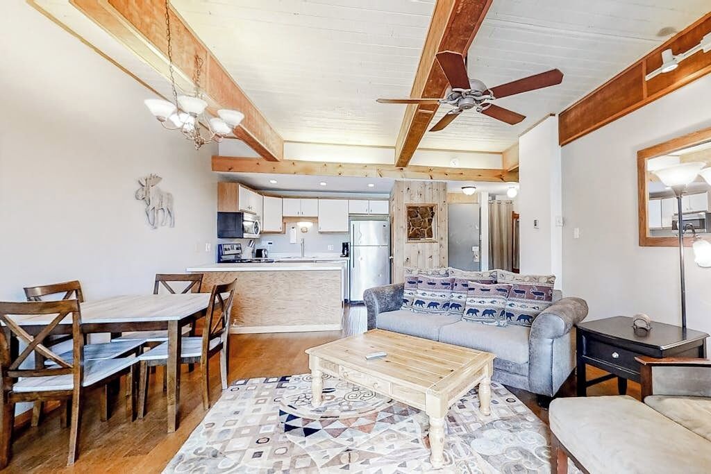 A spacious living area with a sofa, coffee table, and wooden dining set. A ceiling fan and chandelier are visible.