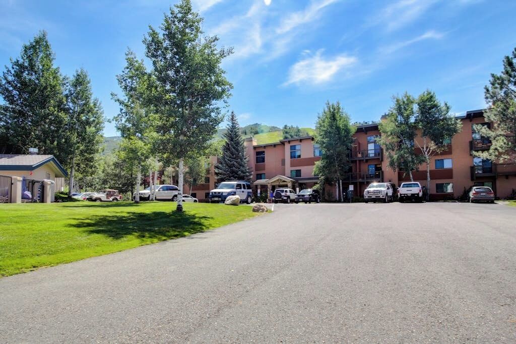 A multi-story building with a parking lot, surrounded by trees and a clear sky.