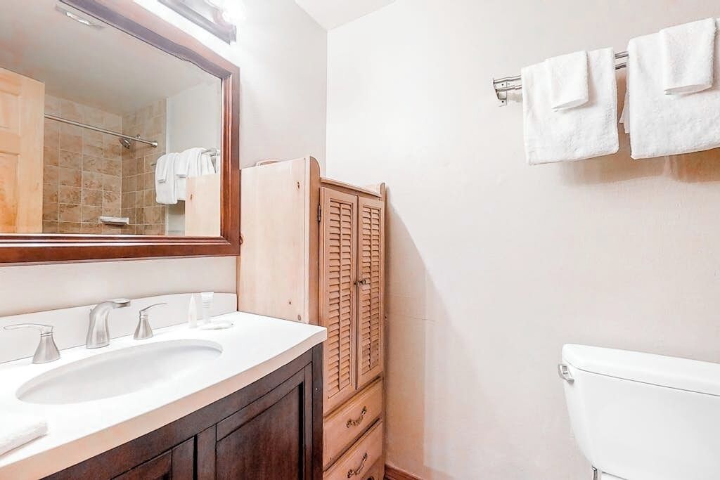 A bathroom with a double sink, a mirror, a toilet, and a wooden cabinet.
