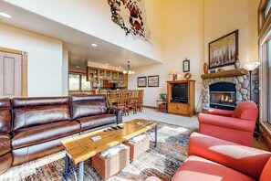 Ein geräumiges Wohnzimmer mit einer Ledersofa, einem roten Sessel, einem Kamin, einem Essbereich und einer Küche im Hintergrund.