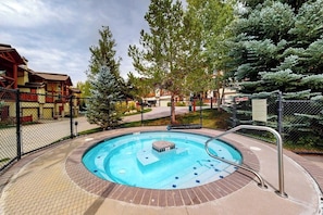 Ein kreisförmiger Pool mit einer Hottube in der Mitte, umgeben von einer Ziegelterrasse und einem Metallzaun.