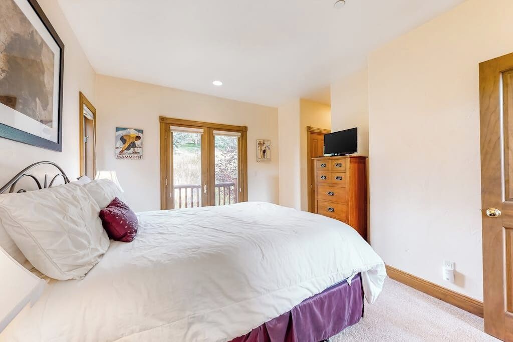 Een slaapkamer met een bed, een dressoir, een televisie en een deur.