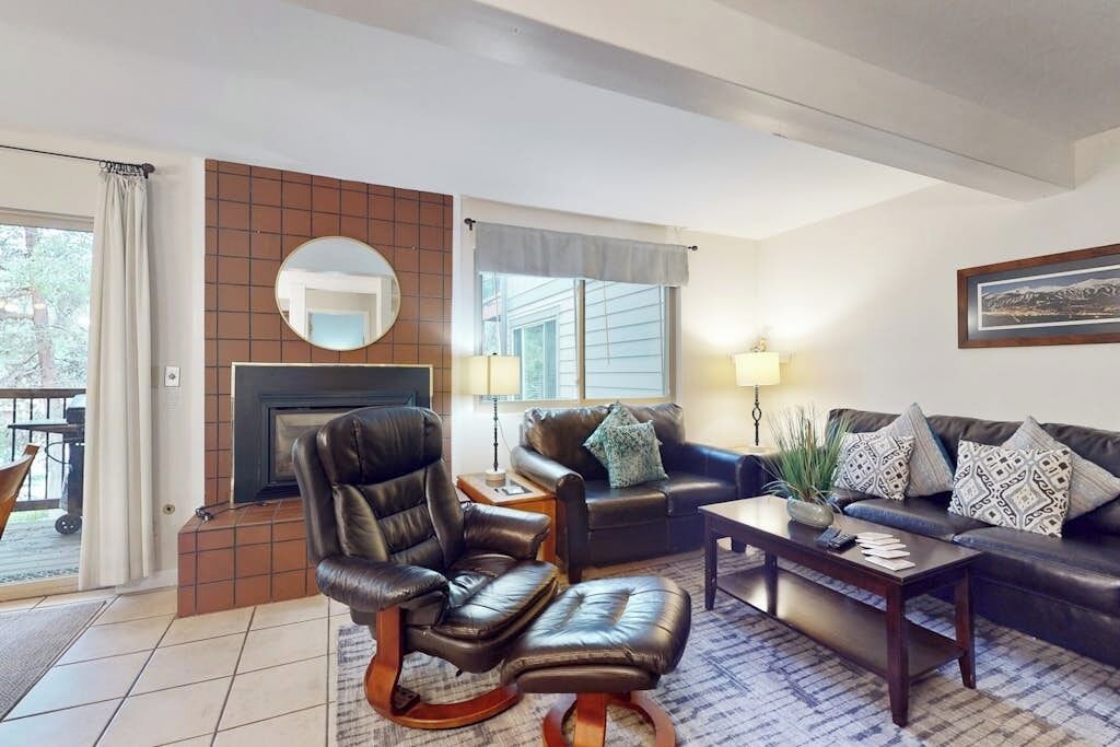 A living room with a fireplace, leather armchair, sofa, coffee table, and a view of the outdoors.