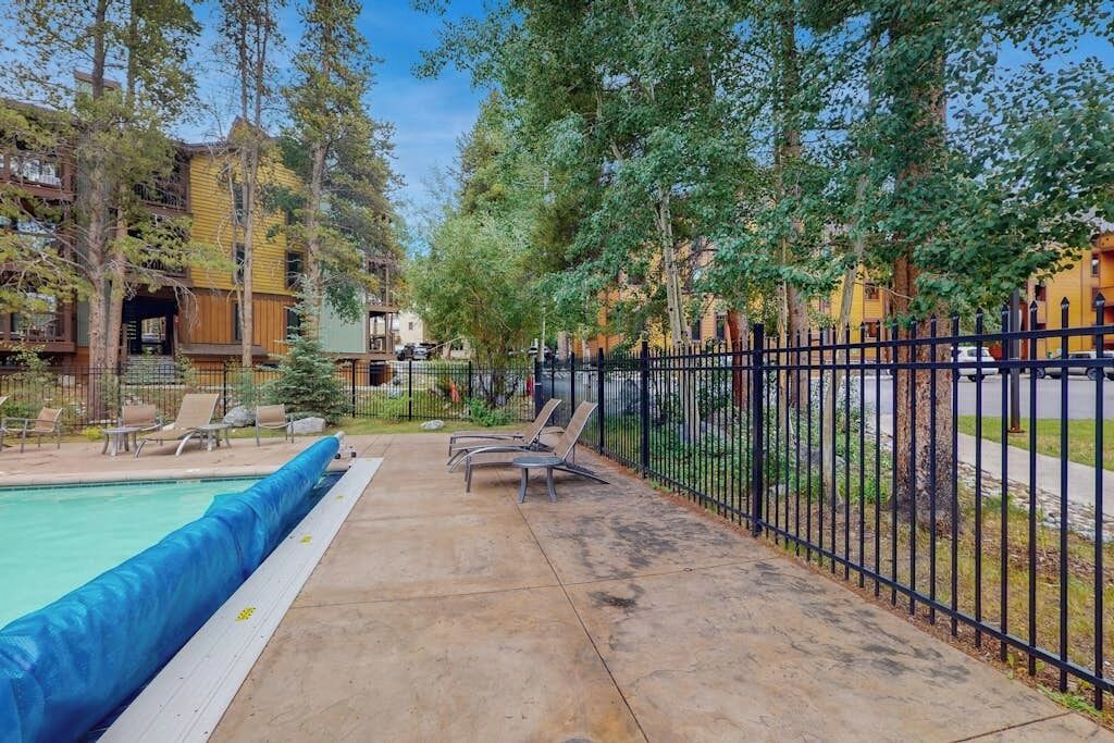 A pool area with lounge chairs, a fence, and buildings in the background.