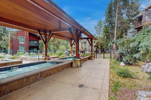 Ein überdachter Poolbereich mit Holz-Pergola, einem Schwimmbecken und einem angelegten Garten mit Bäumen und Sträuchern.