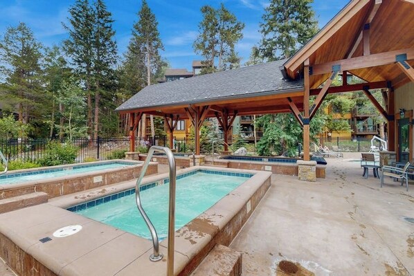 A pool area with a wooden deck, a covered seating area, and a view of surrounding trees. - Serene Breckenridge condo with decks, fireplace, and pool (Breckenridge)