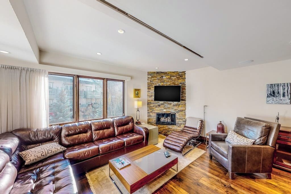A modern living room with a sectional sofa, a fireplace, a flat-screen TV, and a large window.