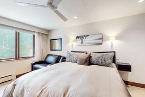 Ein Schlafzimmer mit einem Bett, einem Sessel, einem Deckenventilator, einem Fenster und Wandleuchten.