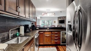 A modern kitchen with dark wooden cabinets, stainless steel appliances, and a large refrigerator. - 1 Block to Vail Mountain! Village Condo w/ Fireplace, Great Views & Shared Pool (Vail)