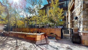 A courtyard with stone walls, a metal gate, and trees. - 1 Block to Vail Mountain! Village Condo w/ Fireplace, Great Views & Shared Pool (Vail)