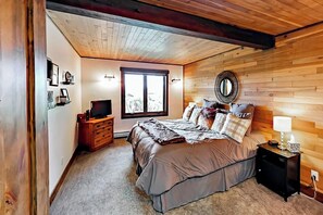 Ein Schlafzimmer mit Holzboden, einem großen Bett mit Kissen, einem Nachttisch, einem Fernseher und einem Fenster.