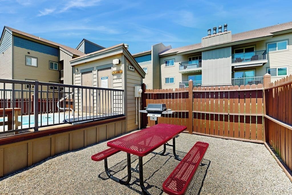 A residential area with a pool, a barbecue grill, and a red picnic table.