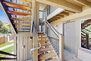 Eine mehrstöckige Holztreppe mit Metallgeländern, eine Tür mit der Aufschrift 'C202' und Blick auf einen Wohnbereich.