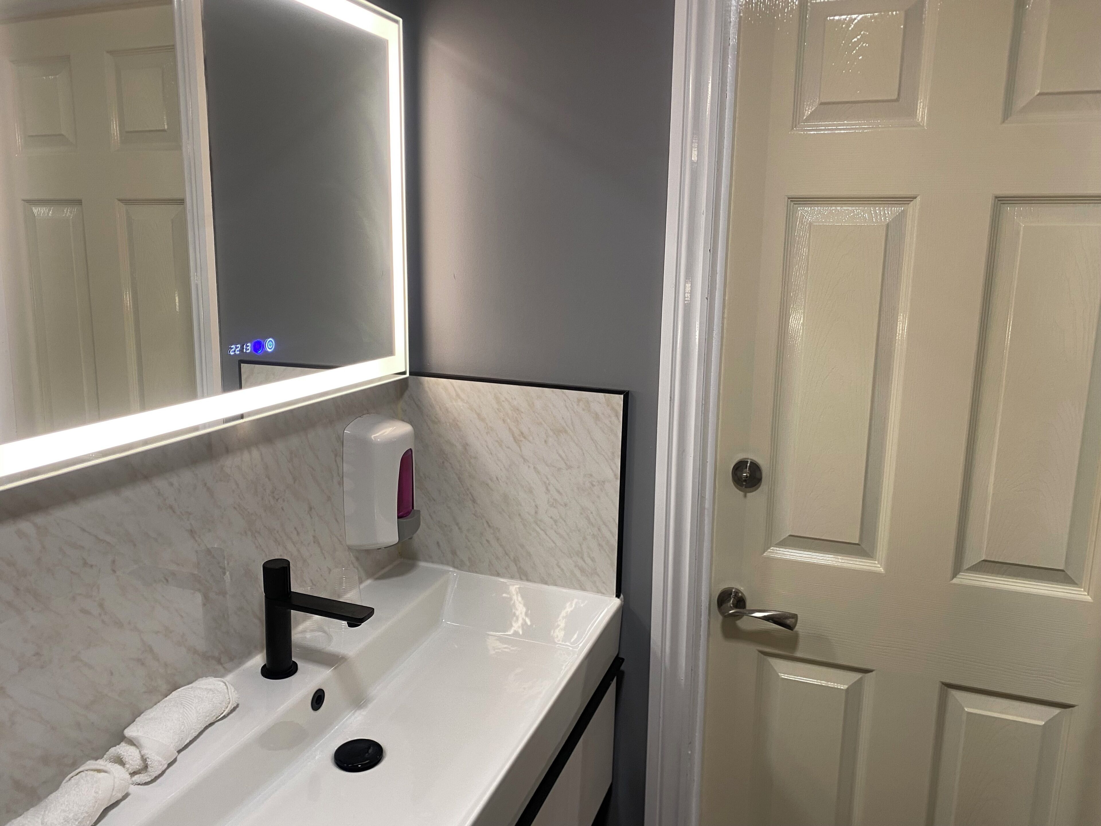 A bathroom with a white sink, a mirror, a soap dispenser, and a towel.