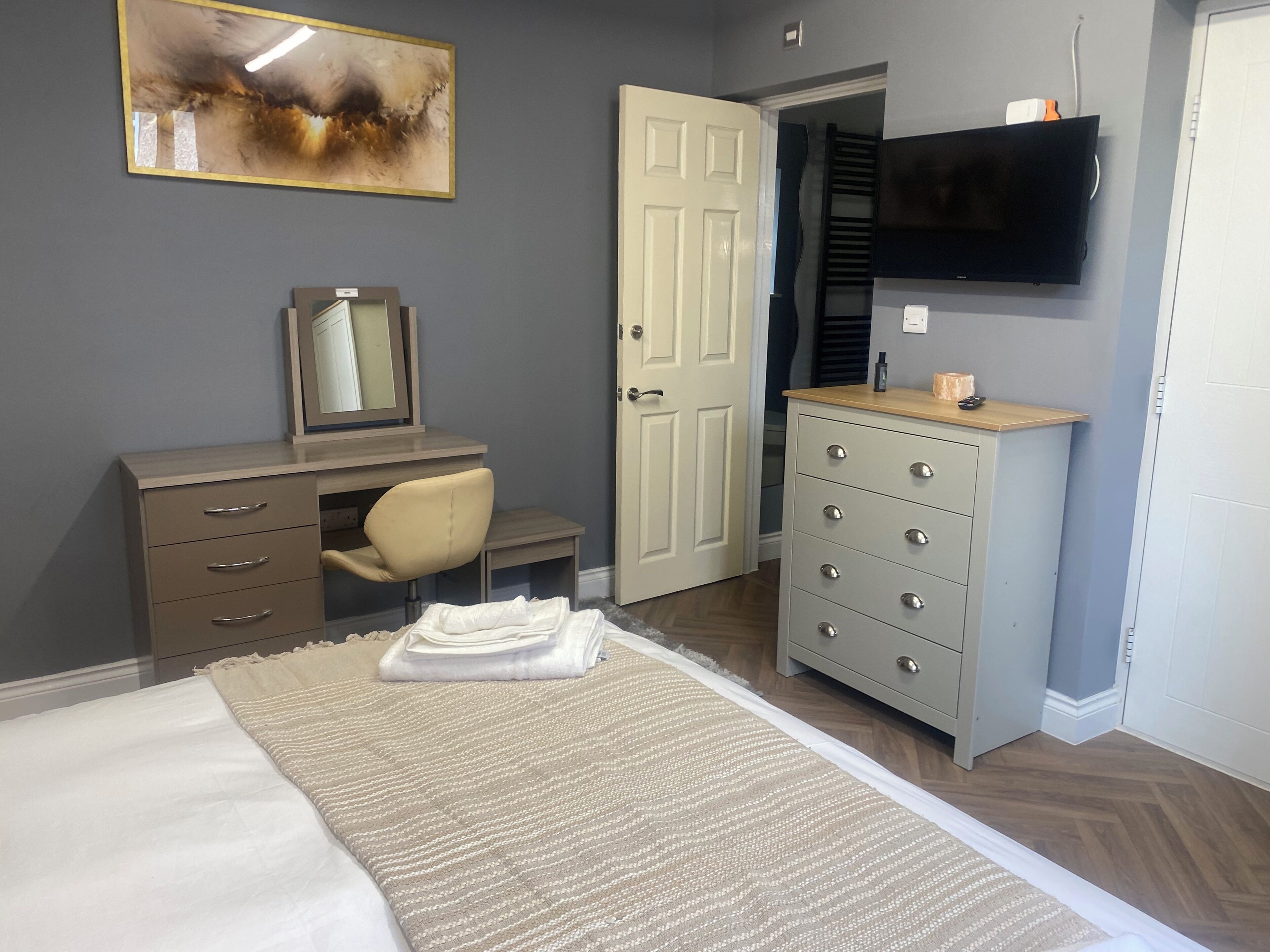 Un dormitorio con cama, cómoda, silla, televisor y puerta.