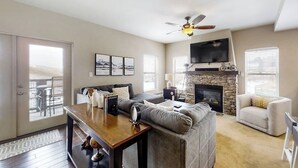 A living room with a fireplace, a ceiling fan, and a television mounted above it. - Family-friendly condo w/mountain & valley views, WiFi, shared pool, hot tub (Granby)