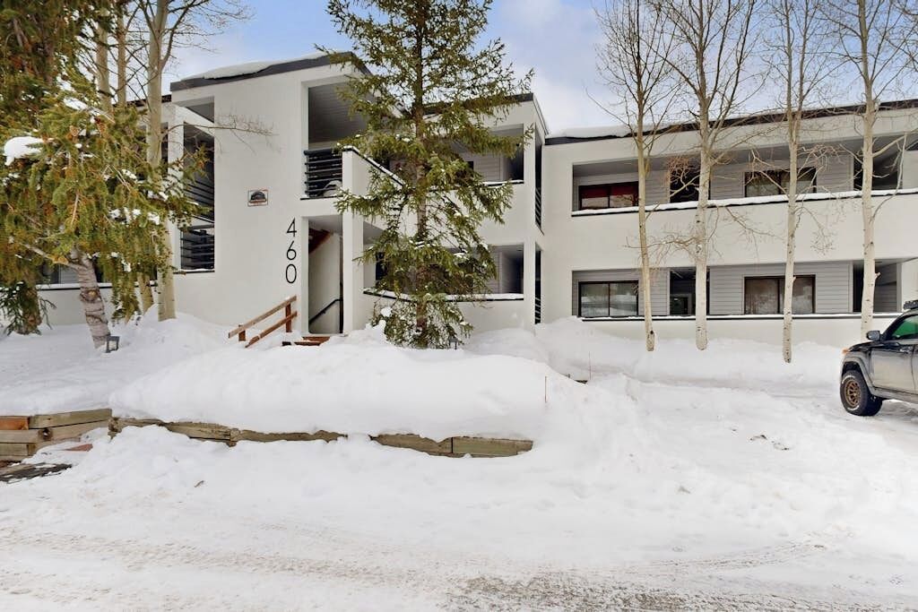 A modern multi-story building with a snow-covered entrance and a parked car.