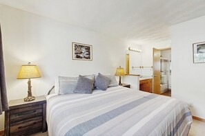 Ein Schlafzimmer mit einem Bett, Nachttischlampen, einem Spiegel und einer Tür zu einem Badezimmer.