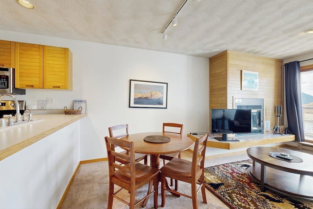 Un salon moderne comprenant un coin repas, une cuisine avec des meubles en bois, un téléviseur à écran plat et une grande fenêtre.