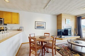 Ein modernes Wohnzimmer mit Essbereich, einer Küche mit Holzausstattung, einem Flachbildfernseher und einem großen Fenster.