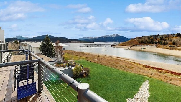 Vista al río con terraza, zona verde y montañas al fondo.