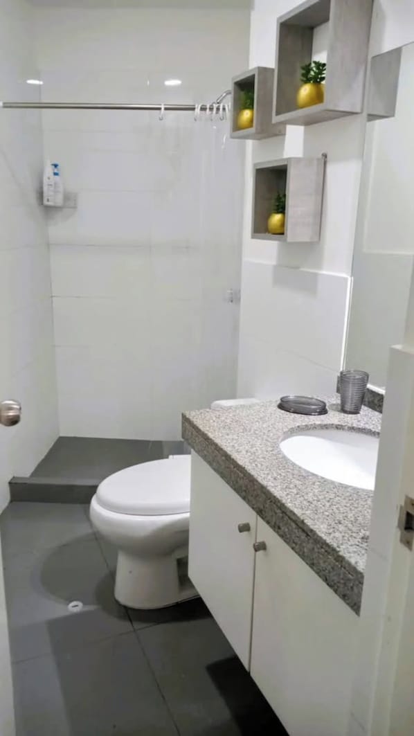Un baño pequeño y moderno con inodoro, lavamanos y zona de ducha.