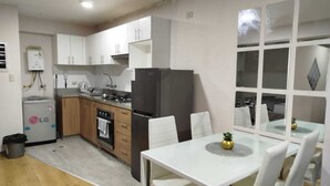A compact kitchen with white cabinets, a black refrigerator, an oven, and a dining table with white chairs. - Central Suite (Lima)